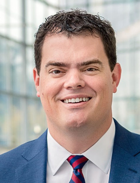 Gabriel White, smiling, wearing a blue suit and a red-and-navy striped tie.